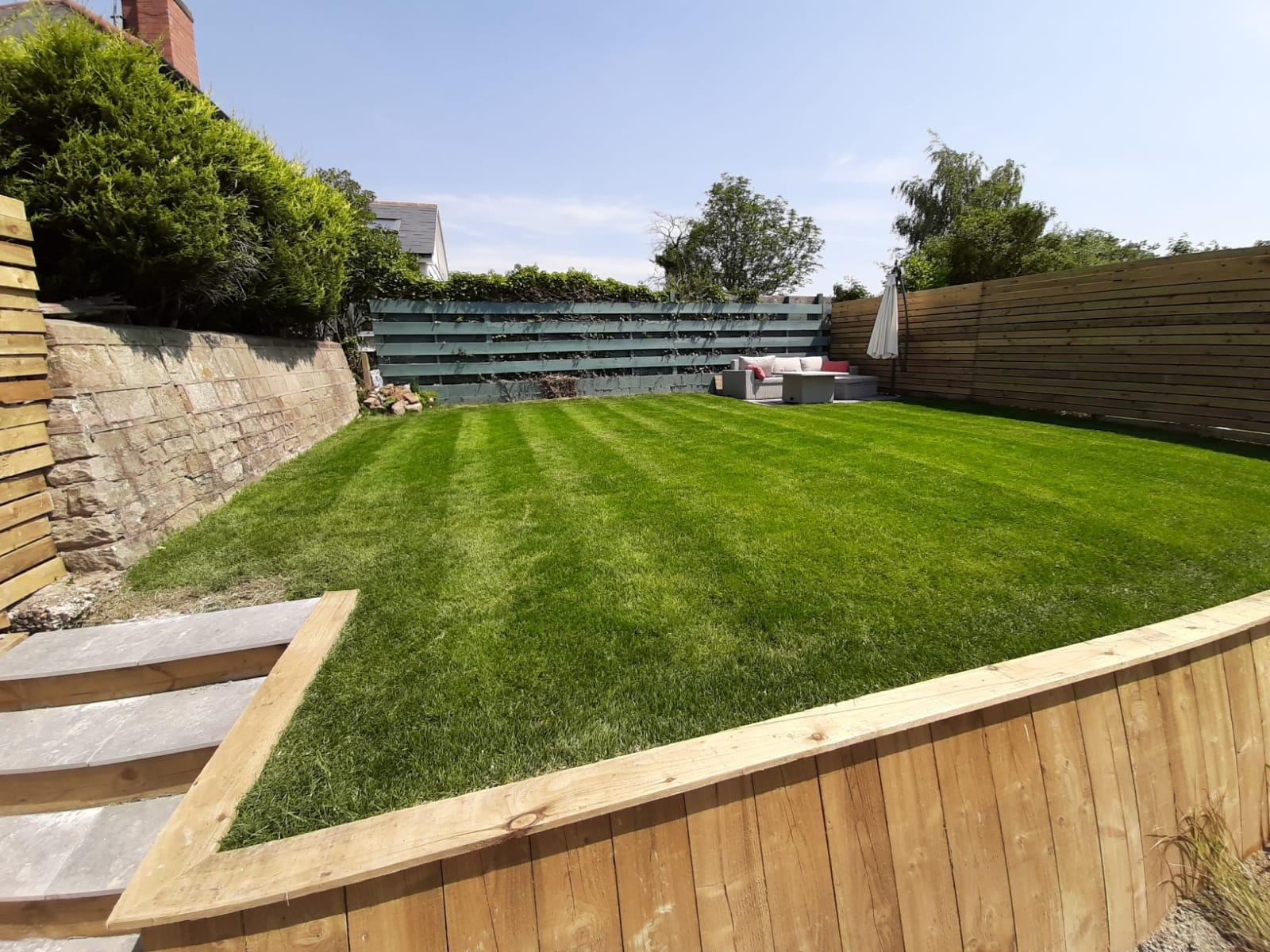 A professionally landscaped garden with a striped lawn and timber retaining walls